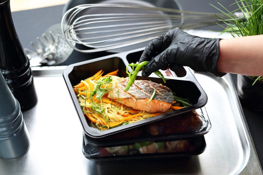 Chef plating salmon into catering trays in a commercial kitchen